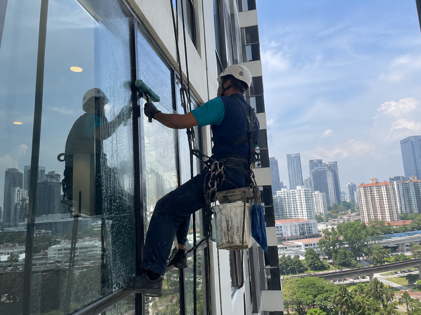Professional worker cleaning high-rise building windows as part of commercial and industrial cleaning services in KL
